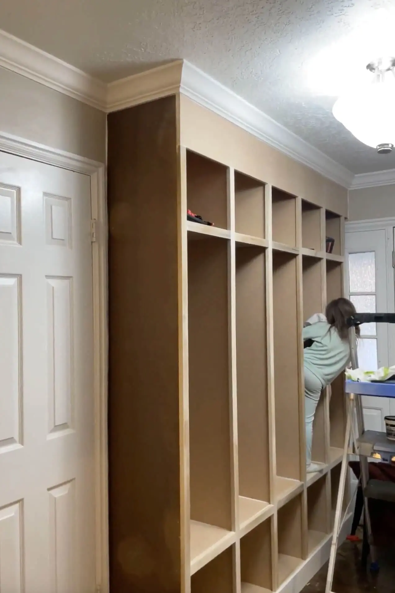A DIYer making final adjustments to the trim of a built-in entryway storage unit, ensuring a professional and polished finish.